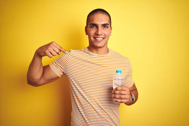 istock Young handsome man holding plastic water bottle over yellow isolated background with surprise face pointing finger to himself 1187204628