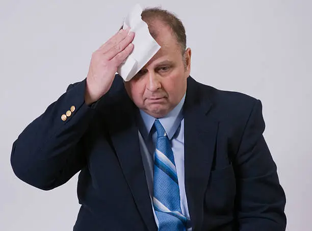 Worried businessman is wiping his forehead.
