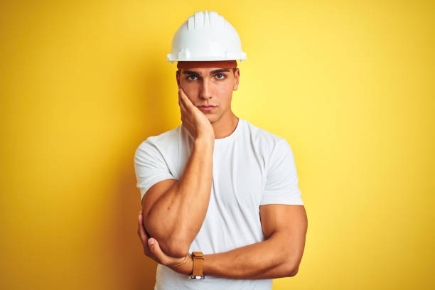 Young handsome man wearing construction helmet over yellow isolated background thinking looking tired and bored with depression problems with crossed arms. Young handsome man wearing construction helmet over yellow isolated background thinking looking tired and bored with depression problems with crossed arms. lazy construction laborer stock pictures, royalty-free photos & images