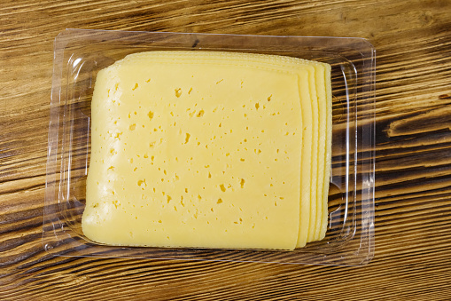 Slices of cheese in disposable plastic packing box on wooden table. Top view