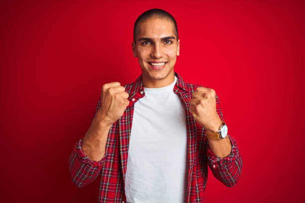 istock Young handsome man wearing a shirt using watch over red isolated background celebrating surprised and amazed for success with arms raised and open eyes. Winner concept. 1187206479