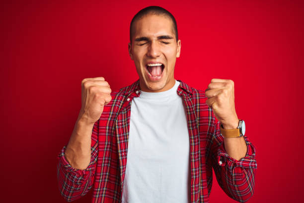 istock Young handsome man wearing a shirt using watch over red isolated background celebrating mad and crazy for success with arms raised and closed eyes screaming excited. Winner concept 1187206591