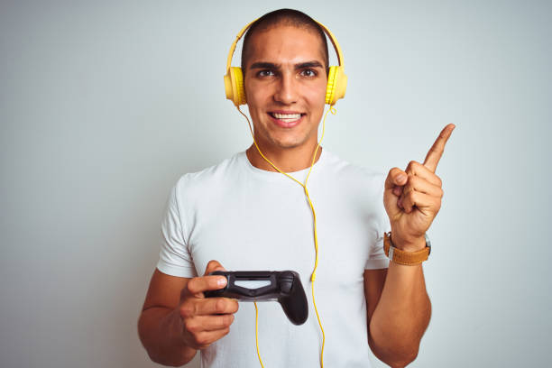 istock Young handsome man playing videogames using headphones over white isolated background very happy pointing with hand and finger to the side 1187208289