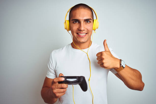 istock Young handsome man playing videogames using headphones over white isolated background happy with big smile doing ok sign, thumb up with fingers, excellent sign 1187208298