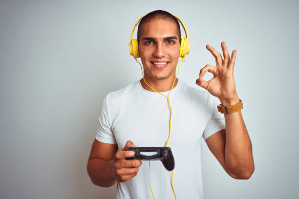 istock Young handsome man playing videogames using headphones over white isolated background doing ok sign with fingers, excellent symbol 1187208356