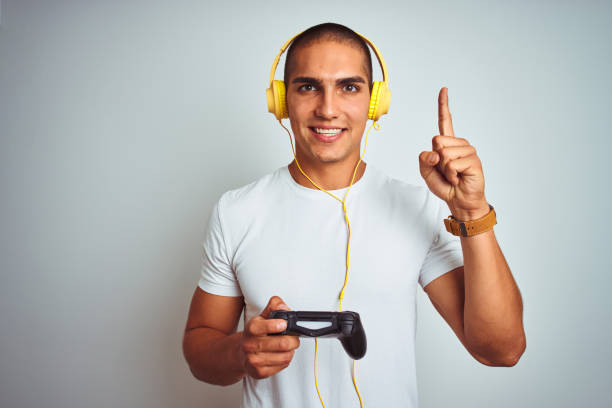 istock Young handsome man playing videogames using headphones over white isolated background surprised with an idea or question pointing finger with happy face, number one 1187208479