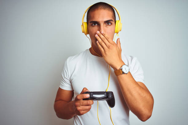 istock Young handsome man playing videogames using headphones over white isolated background cover mouth with hand shocked with shame for mistake, expression of fear, scared in silence, secret concept 1187208483