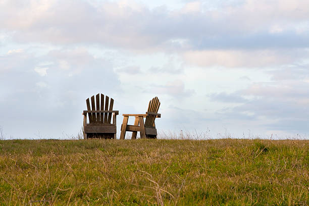 Due sedie in legno in un campo con sky. - foto stock