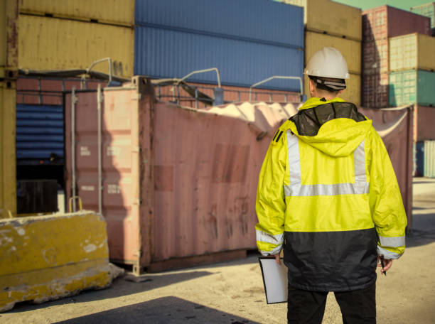 istock Ship supervisor engineer inspector stands at the dockside near to damaged ship container. Wearing safety helmet and yellow vest. Cargo shipping industry. 1187216704