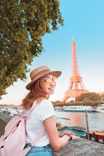 Happy asian woman student with backpack observing view of the Eiffel Tower in Paris. Travel and education in France concept