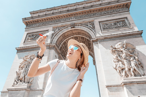 Girl traveler playing with a toy airplane on the background of the arc de Triomphe. The concept of low-cost and cheap airline tickets for students and tourists.