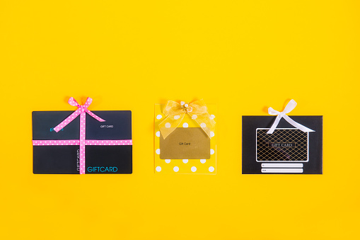 Gift card concept. Top view Shop gift cards in shape of present boxes with satin ribbons on bright yellow background. Creative ideas for presents. Flat lay. Holiday sales mockup with copy space