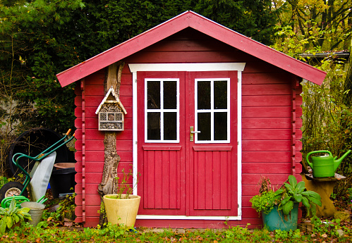 Un pequeño cobertizo rojo claro, casa de jardín, con algunas herramientas de jardín a su alrededor photo