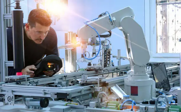 Photo of Man is programming robotic arm with control panel which is integrated on smart factory production line. industry 4.0 automation line which is equipped with sensors and robotic arm