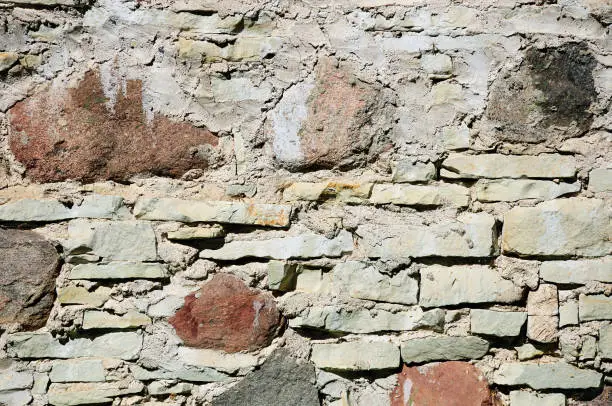 Fragment of wall made of rough uneven stones of different types: granite, flagstone, limestone
