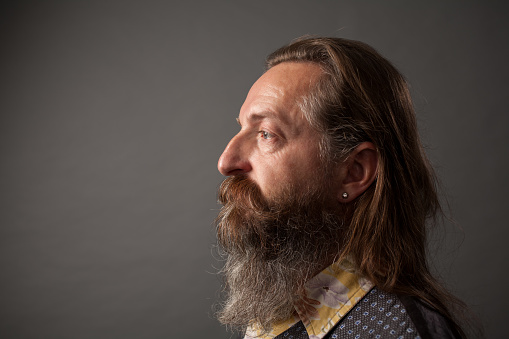Studio portrait of a 50 year old bearded man with long hair in a shirt and waistcoat on a gray background