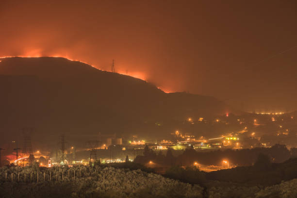 a massive wildfire burns its way in to grand coulee washington at night. the fire and the city glow in the smoke night air. silhouettes of the power line towers that connect the grand coulee dam can be clearly seen. - 7585 imagens e fotografias de stock