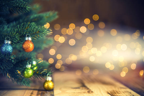 Fir tree decorated with Christmas balls on rustic wood floor and defocused lights in the background