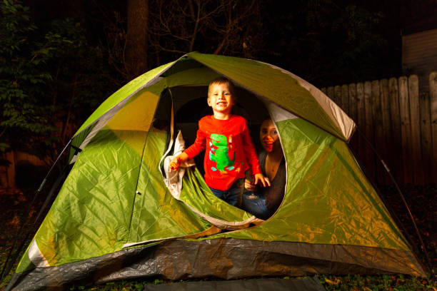 2 Little Boys Play Together With Their Moms in their Backyard in a Green Camping Tent At Night stock photo