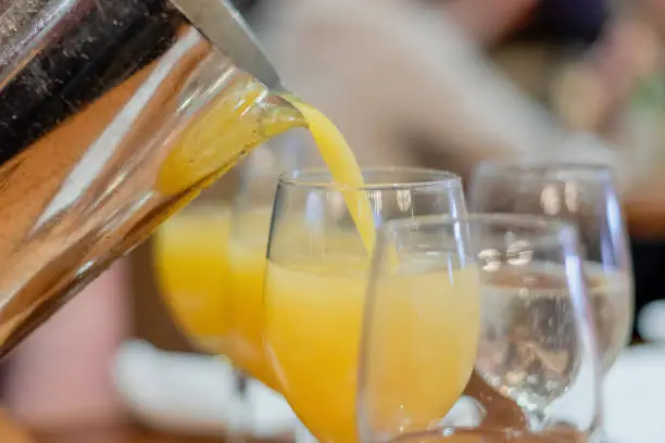 Adding a splash of fresh orange juice to champagne - serving mimosas at brunch