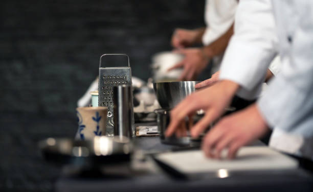 Team of professional chefs preparing food in a commercial kitchen. Team of professional chefs preparing food in a commercial kitchen. Cooks in the production process of system catering. An inside view of a pro catering kitchen in Spain. Extreme narrow depth of field. chefs whites stock pictures, royalty-free photos & images