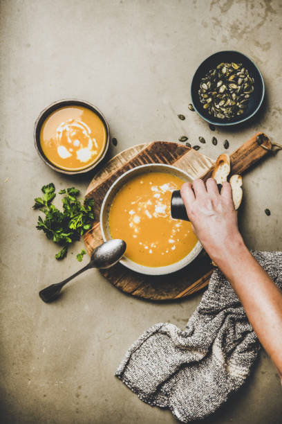 mano de hombre añadiendo pimienta a la sopa de crema de calabaza con semillas - smooth part of colors yellow fotografías e imágenes de stock