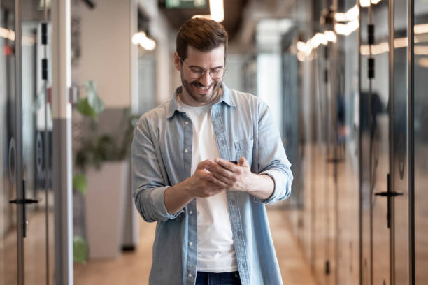 istock Smiling businessman using phone apps, standing in office hallway 1187245889
