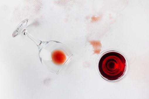 a glass of red wine and an overturned glass with the remains of wine on a white background drenched and stained with wine, top view