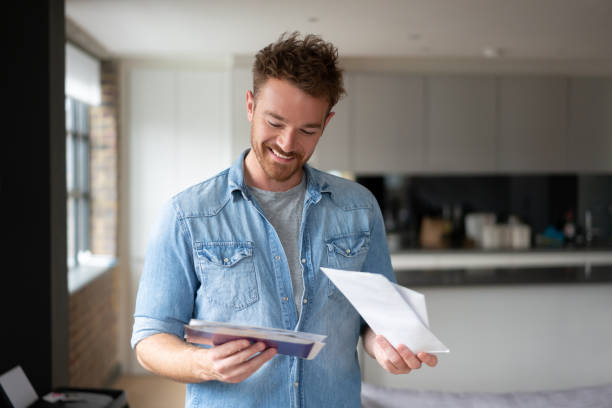 homme heureux à la maison vérifiant le courrier - service postal photos et images de collection