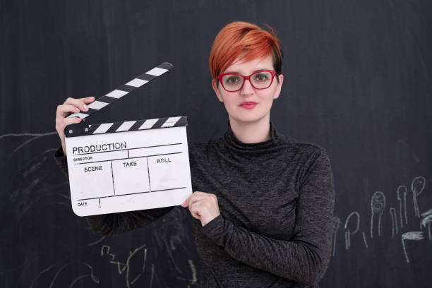 istock redhead woman holding clapper on black background 1187252531