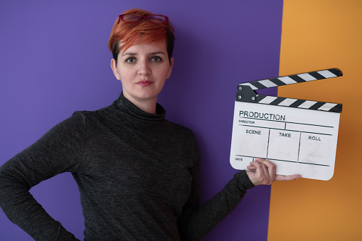 redhead woman holding movie clapper against purple  background  cinema concept