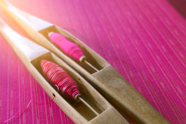Pink yarn in weaving shuttle tool on traditional handmade fabric. Textile weaving. Weaving using traditional weaving loom and shuttle.Textile production in Thailand. Asian culture. OTOP product.