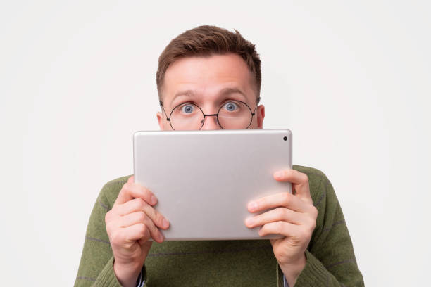 istock Young guy in funny glasses hiding his face with e-book reader 1187256186