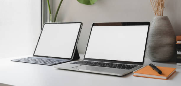 istock Modern office room with open blank screen laptop computer and digital tablet on white wooden table 1187258482