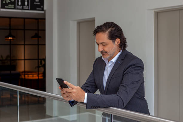 istock A Senior Latin American Company Manager Is Seen Checking Messages On His Mobile Phone While Waiting For His Visitor To Arrive In The Lobby, On The Floor Of His Office Building; In The Background is The Door To The Elevators. Copy Space. 1187260025