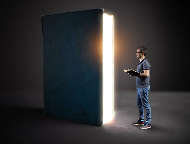 istock Young man holding book and looking magic illuminated big old book 1187264432