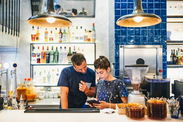 Know your business, grow your business Shot of a man and woman using a digital tablet together while working in a bar busy restaurant tables stock pictures, royalty-free photos & images