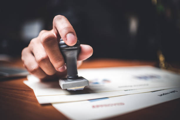 Close-up Of A Person's Hand Stamping With Approved Stamp On Text Approved Document At Desk,  Contract Form Paper
