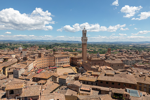 Panoramic view of Siena city with Piazza del Campo and the Torre del Mangia is a tower in city from Siena Cathedral (Duomo di Siena). Summer sunny day and dramatic blue sky