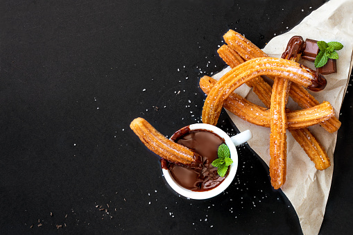 Churros with a cup of hot chocolate on black background. top view. Churro sticks closeup