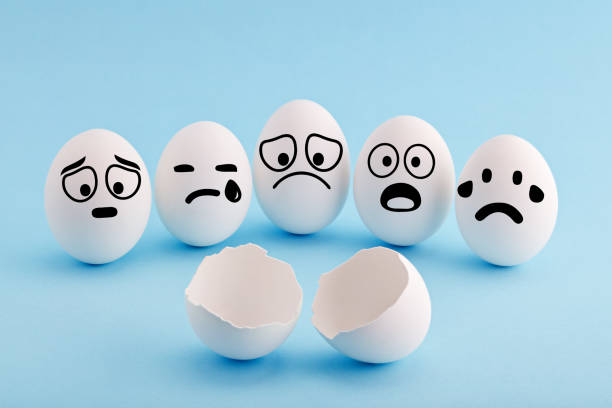 istock White chicken eggs with faces gathered around a broken egg shell and mourning with sad and shocked facial expressions 1187286653