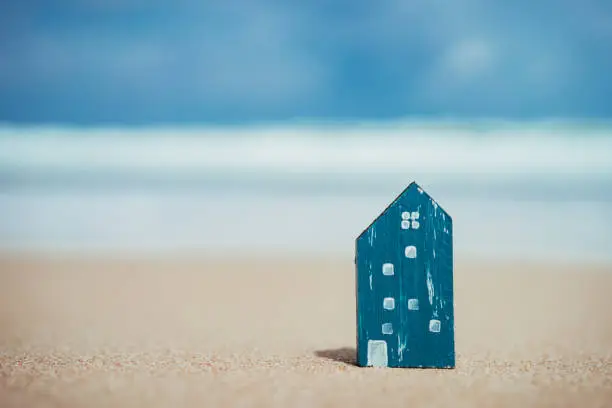Small home model on sand beach with blue sky and white clouds background. Copy space of family lifestyle and business real estate concept. Vintage tone filter effect color style.