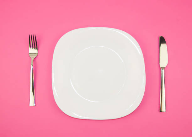 istock White empty plate and knife with a fork on a pink background 1187294339