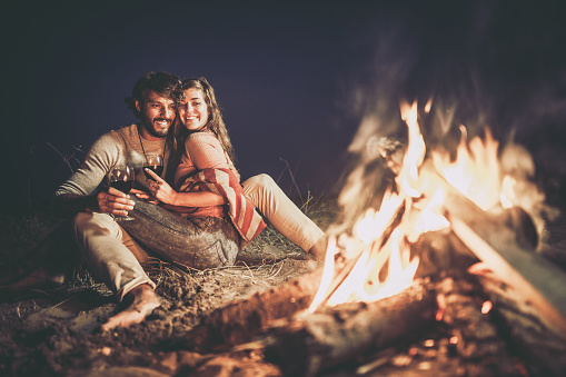 Young happy couple relaxing on the beach by the campfire at night.