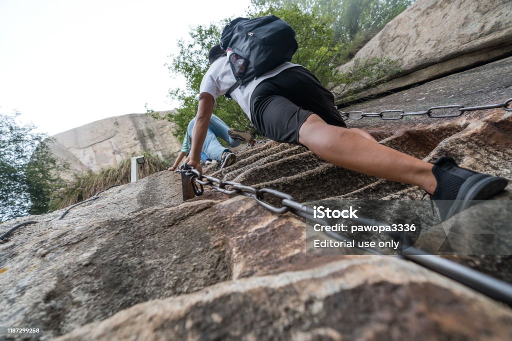 Climber tackling steep stone stairs on Huashan mountain Huashan, China -  August 2019 : Tourist with backpack climbing up the steep, cut into rocky edge stairs on a mountain trail to the North and West Peak on Huashan mountain, Xian, Shaanxi Province Activity Stock Photo