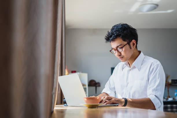 giovane uomo d'affari asiatico che lavora con il computer portatile mentre è seduto nel caffè della caffetteria - indonesia foto e immagini stock