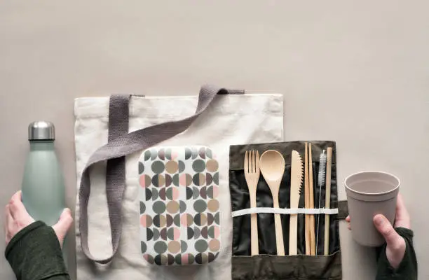 Creative top view, zero waste packed lunch concept, takeaway lunch box set with bamboo cutlery, reusable box, cotton bag and hand with coffee-to-go cup. Sustainable lifestyle, flat lay on craft paper.