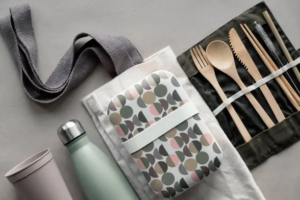 Creative top view, zero waste packed lunch kit, takeaway lunch box set on cotton bag, organizer of bamboo cutlery, reusable box and coffee-to-go cup. Sustainable lifestyle, flat lay on craft paper.