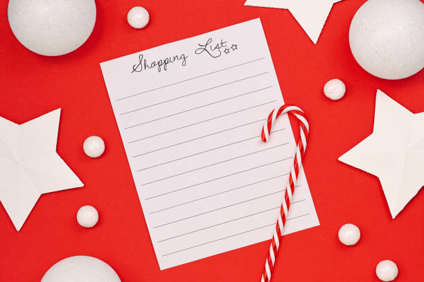 Concept for Christmas shopping with top view flat lay with empty shopping check list and seasonal decorations like candy cane, snow and stars on bright red background