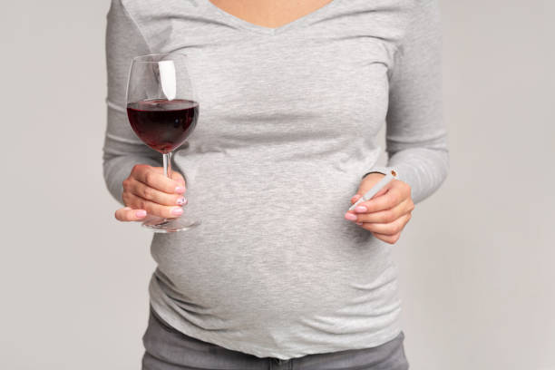 donna incinta che tiene sigaretta e vino in piedi su sfondo grigio - abdomen addiction adult alcohol foto e immagini stock